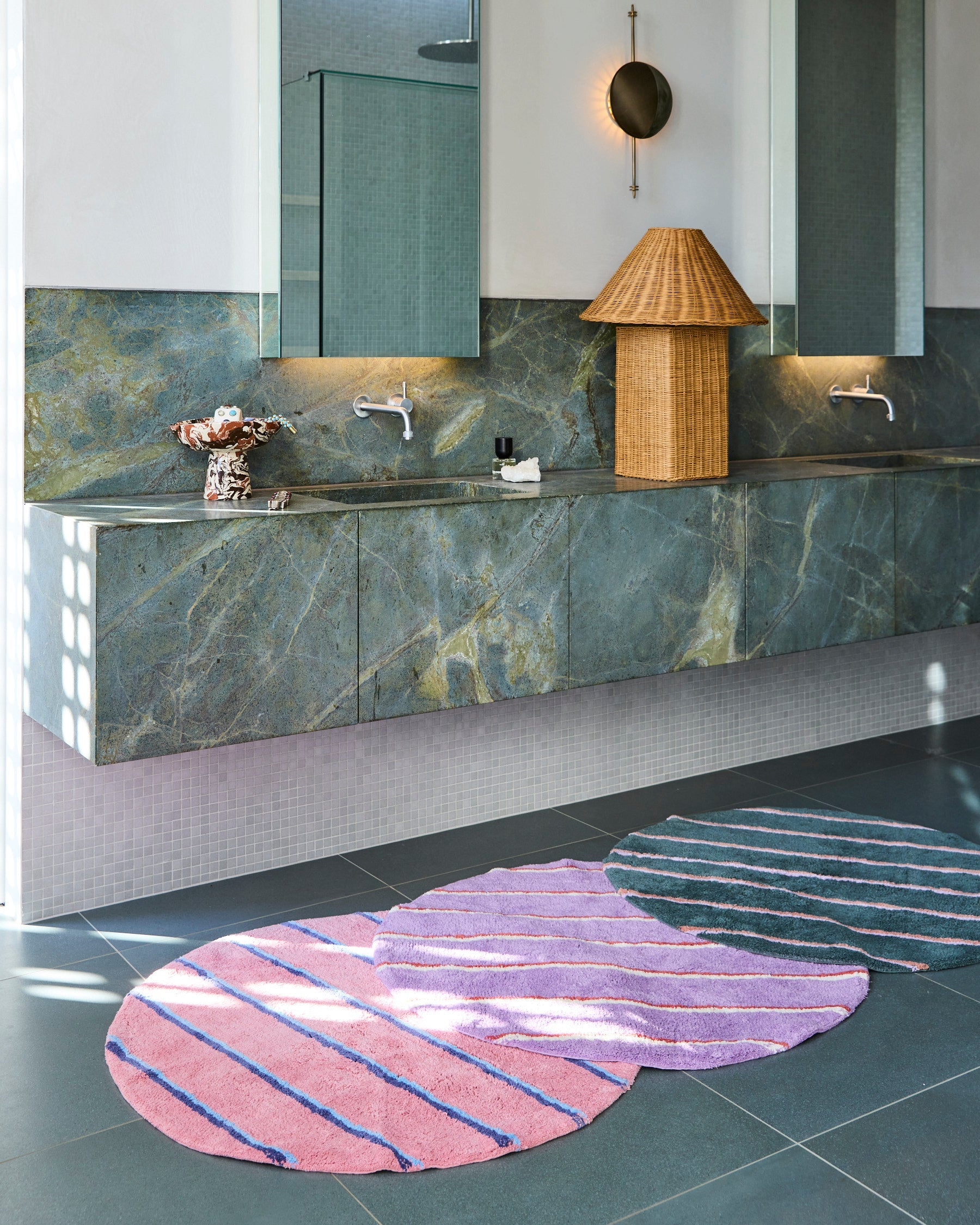 Modern bathroom setting showing Kip & Co Blushing Stripe Round Bath Mat with wicker basket and marble features
