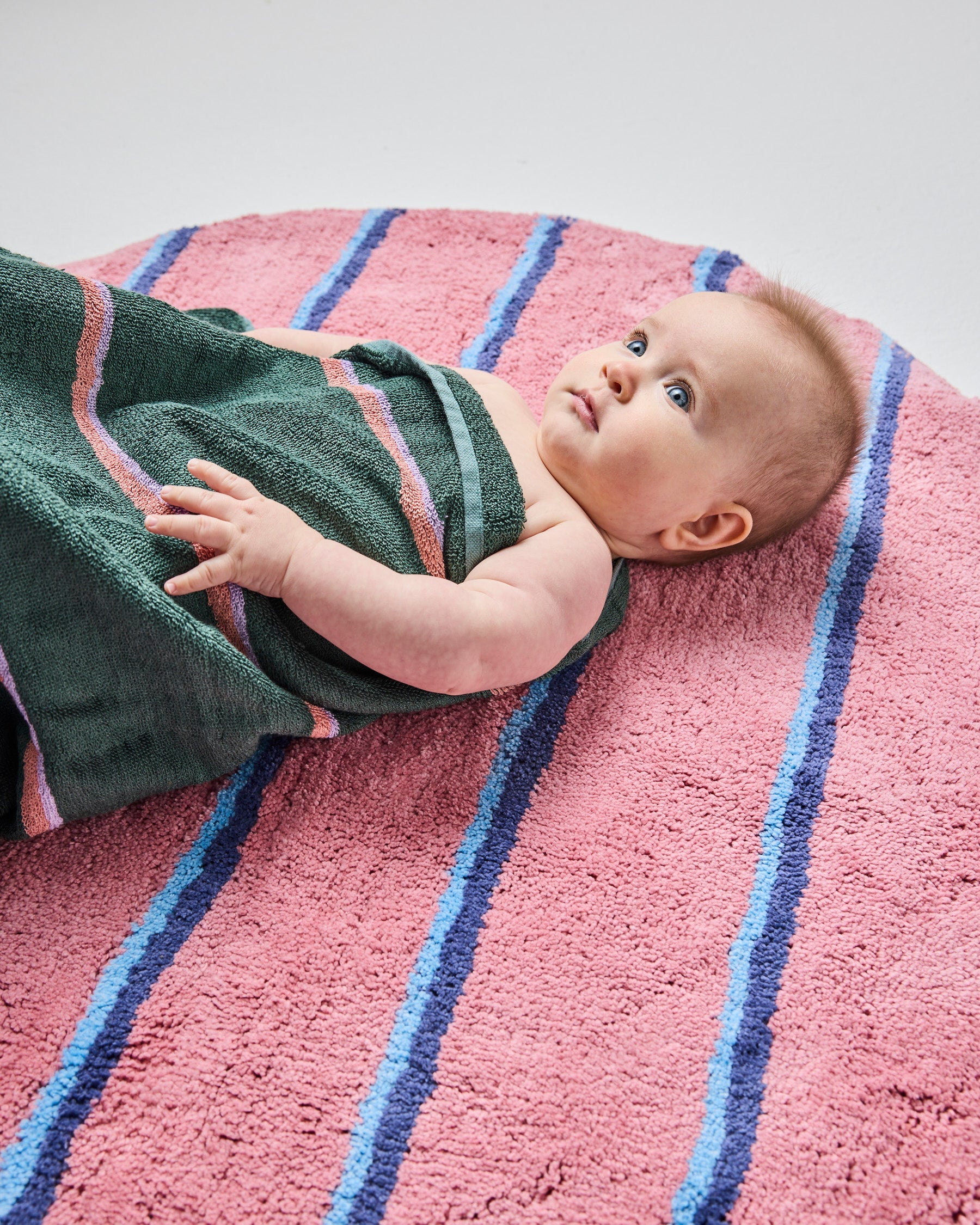Close-up of baby on Kip & Co Blushing Stripe Bath Mat with green towel showing comfortable texture