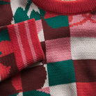 Close-up of Bodhi Kids knit sweater fabric showing colorful checkered pattern and red ribbed cuff detail