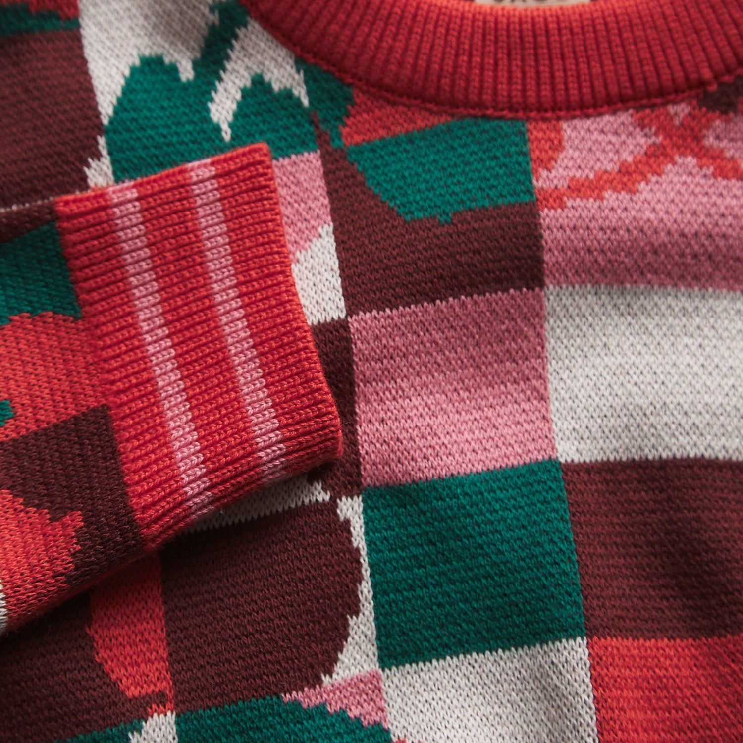 Close-up of Bodhi Kids knit sweater fabric showing colorful checkered pattern and red ribbed cuff detail