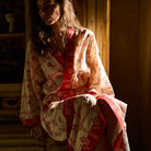 Bonny Cotton Robe in Poppy — cream cotton with red floral check pattern and wide red border, seated close-up view