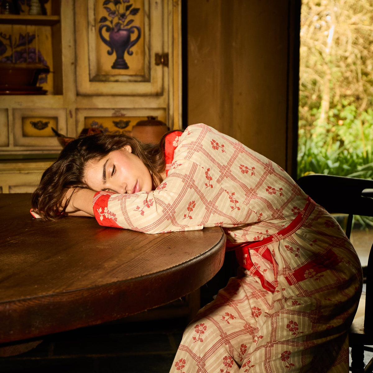Bonny Cotton Robe in Poppy — red and cream floral check print with red cuff trim, shown from above on reclining model