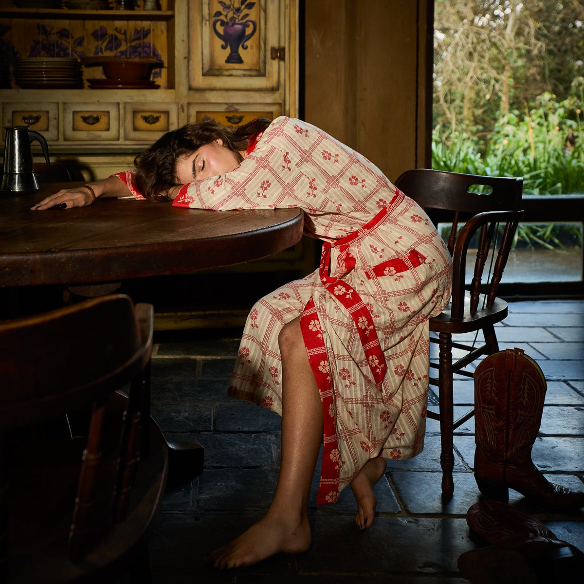 Bonny Cotton Robe in Poppy — full-length view of red and cream floral check print robe on reclining model at table