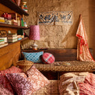 Poppy Bonny Cotton Robe draped over a bench in a rustic room, showing red floral check print and border trim