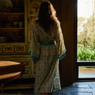 Bonny Cotton Robe in Turquoise — back view on model walking toward doorway, turquoise trim and floral check print