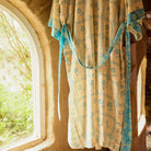 Turquoise Bonny Cotton Robe hanging by an arched window, showing floral check print and turquoise tie belt