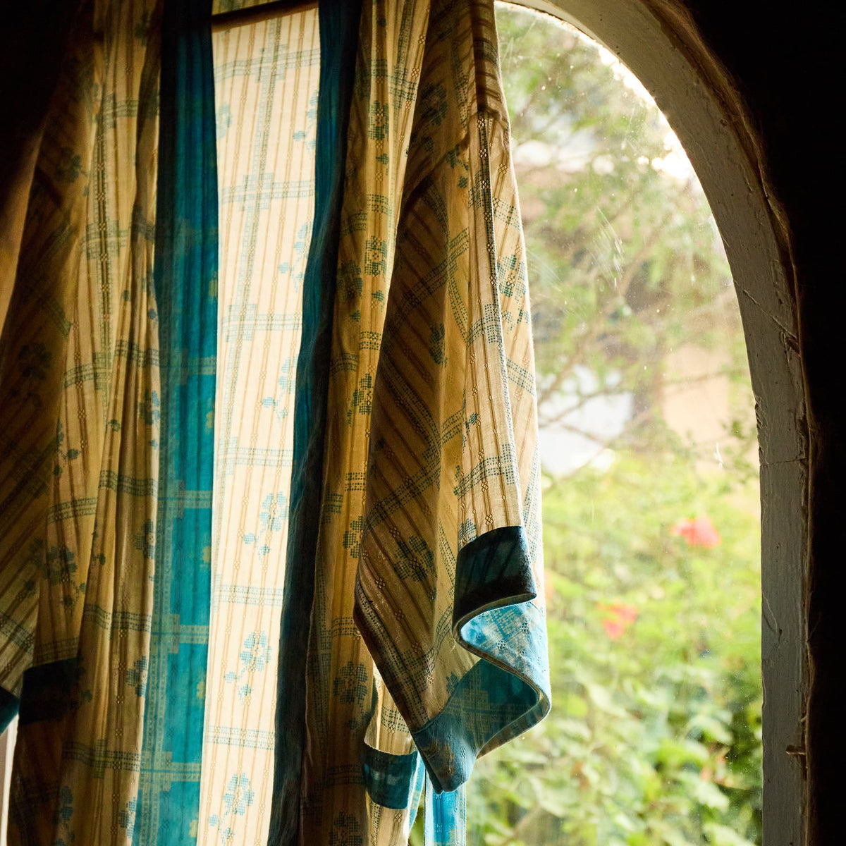 Turquoise Bonny Cotton Robe hanging at an arched window, close-up of floral check print and turquoise cuff trim