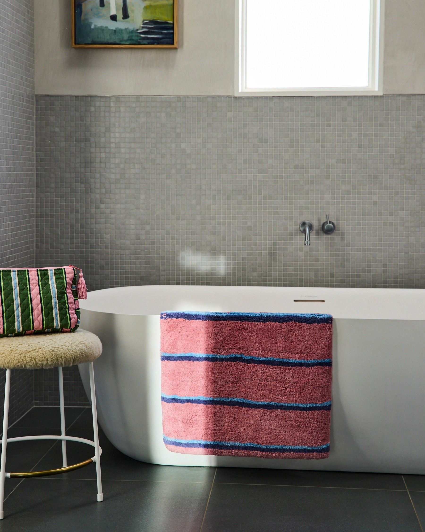 Cactus Stripe toiletry purse positioned on bathroom stool beside white bathtub in modern tiled bathroom setting