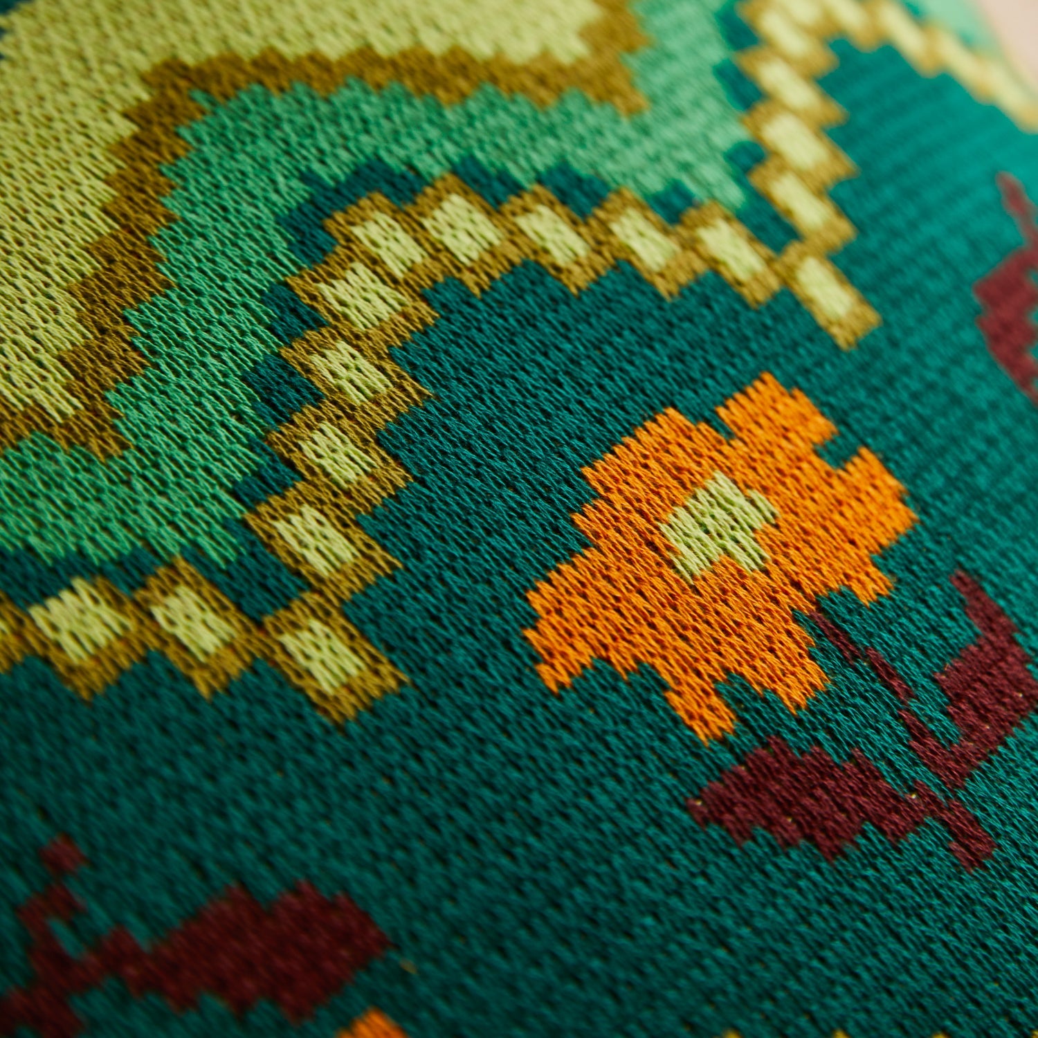Close-up of knit fabric texture showing orange and burgundy floral details on green Calina cushion