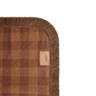 Corner detail of Camp Picnic Rug showing brown fringe trim and hemp gingham fabric texture