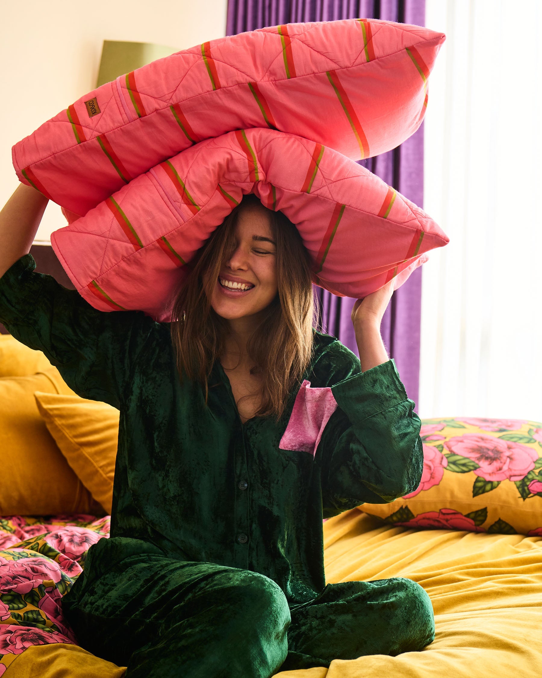 Model holding pillow wearing Candy Pine velvet pyjama set showing playful bedroom styling