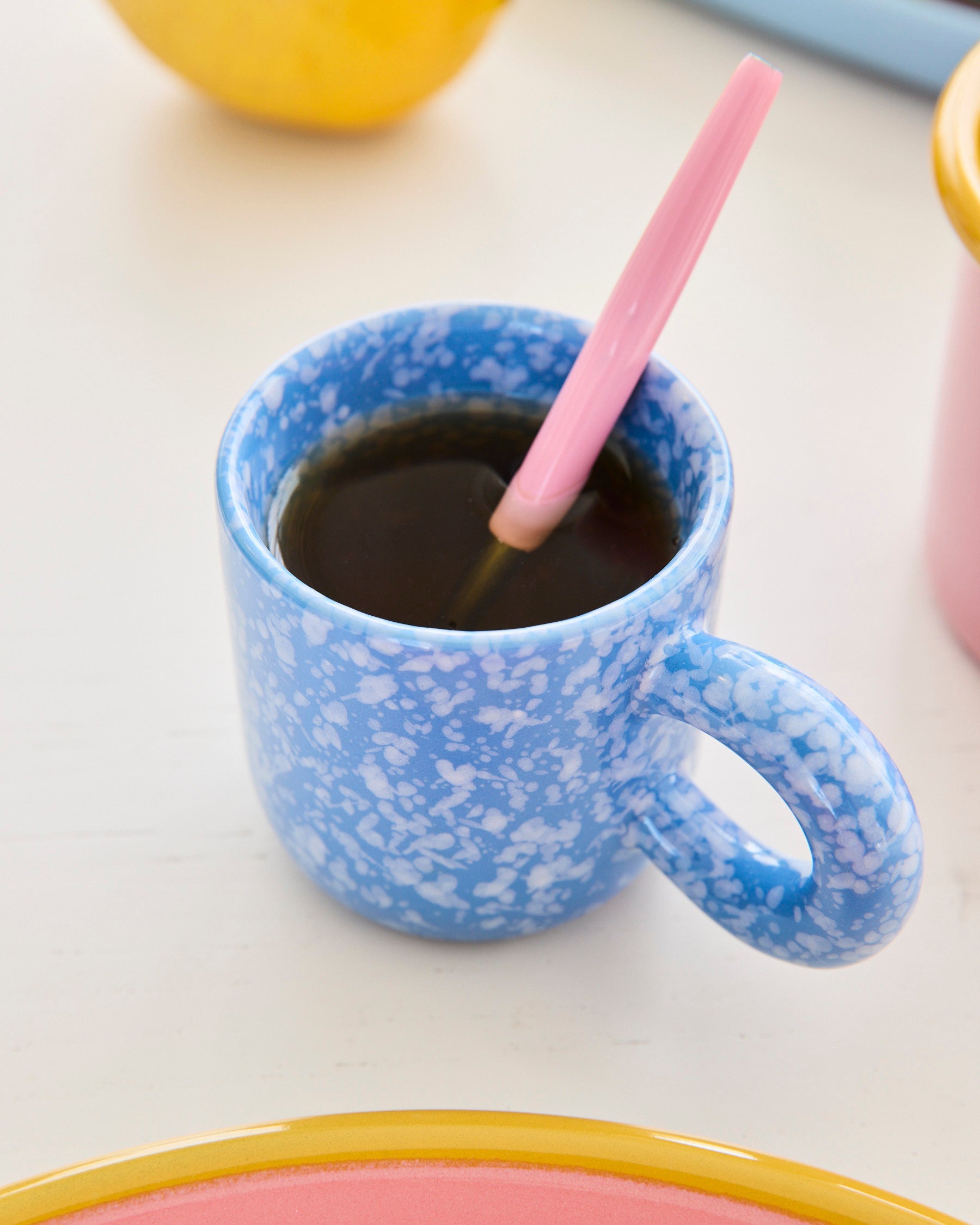 Single blue marbled espresso mug filled with coffee and pink straw on colorful table setting