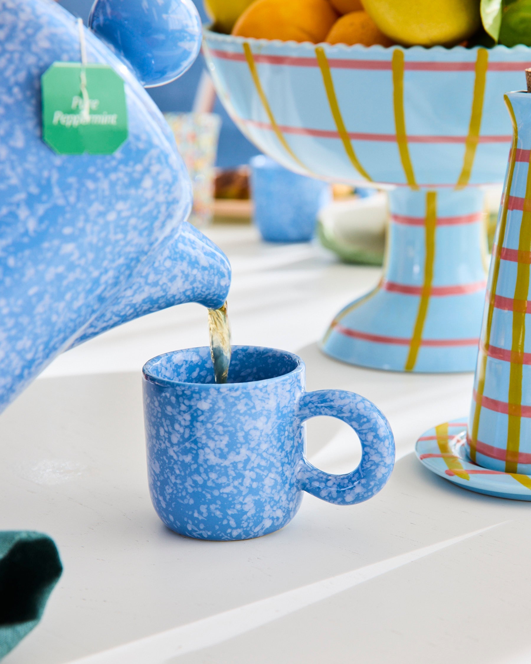 Blue speckled ceramic teapot pouring into matching espresso mug showing marbled glaze finish