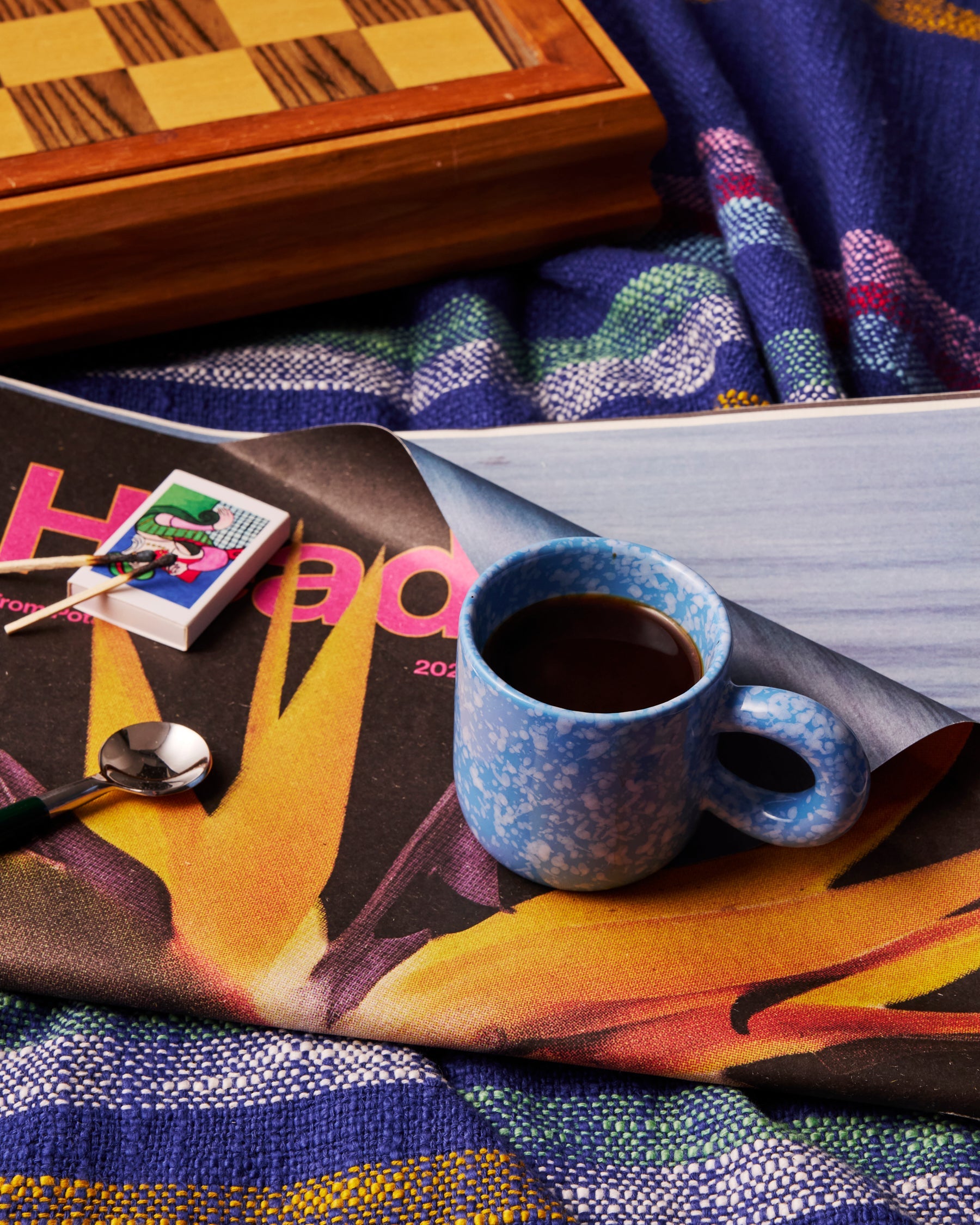 Blue marbled espresso mug with coffee on vintage magazine surrounded by colorful textiles