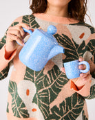 Woman holding blue speckled ceramic teapot and matching espresso mug demonstrating 2P set