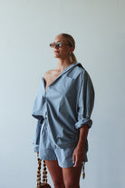 Woman wearing a blue outfit with sunglasses against a plain background