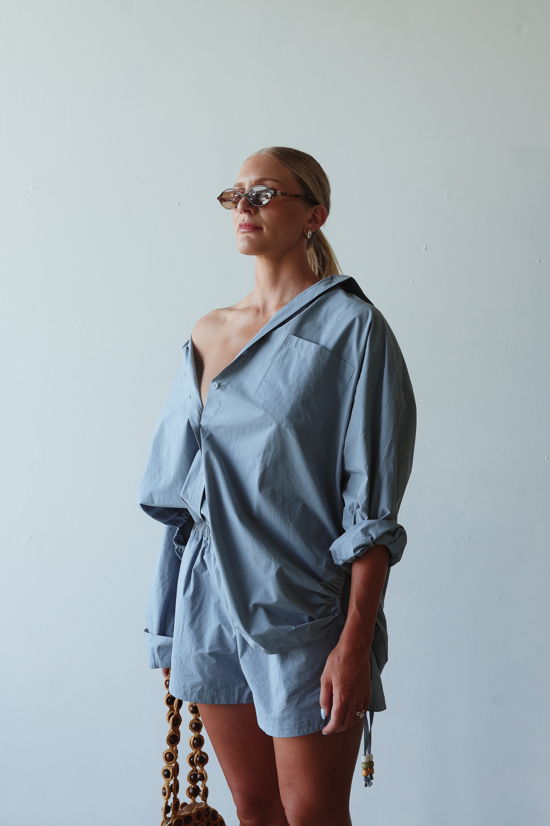 Woman wearing a blue outfit with sunglasses against a plain background