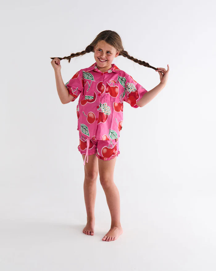 girl wearing Cherry Blossom Kids Organic Cotton Short Sleeve Shirt & Short Pyjama Set by Kip & Co - pink pj's with red cherries