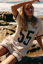 lady wearing organic cotton pointelle fabric cream shirt with brown "55" on the front. 