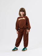 Front view of brown embroidered sweater with golden ace text and long sleeves on matching brown tracksuit