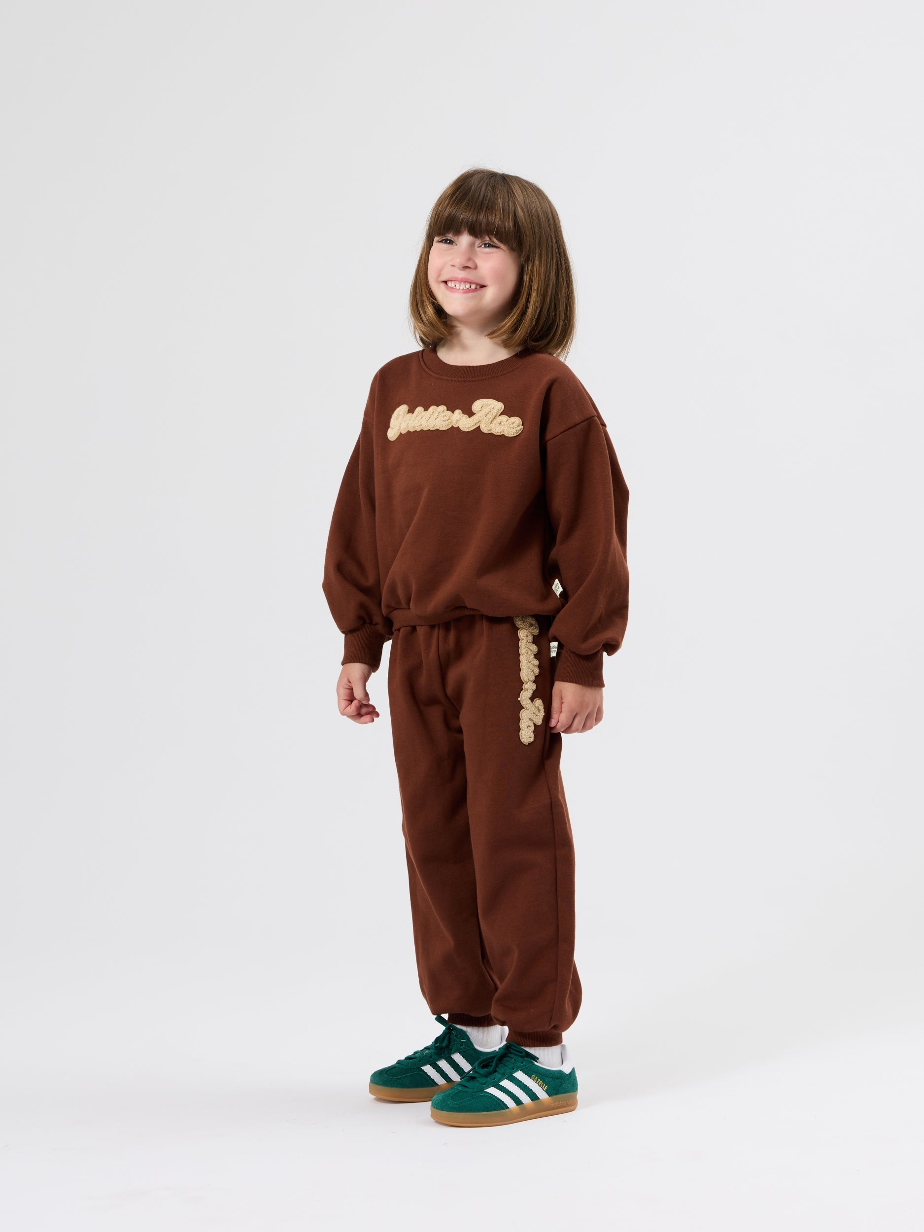 Full length view of brown embroidered sweater with golden ace embroidery worn with matching brown sweatpants