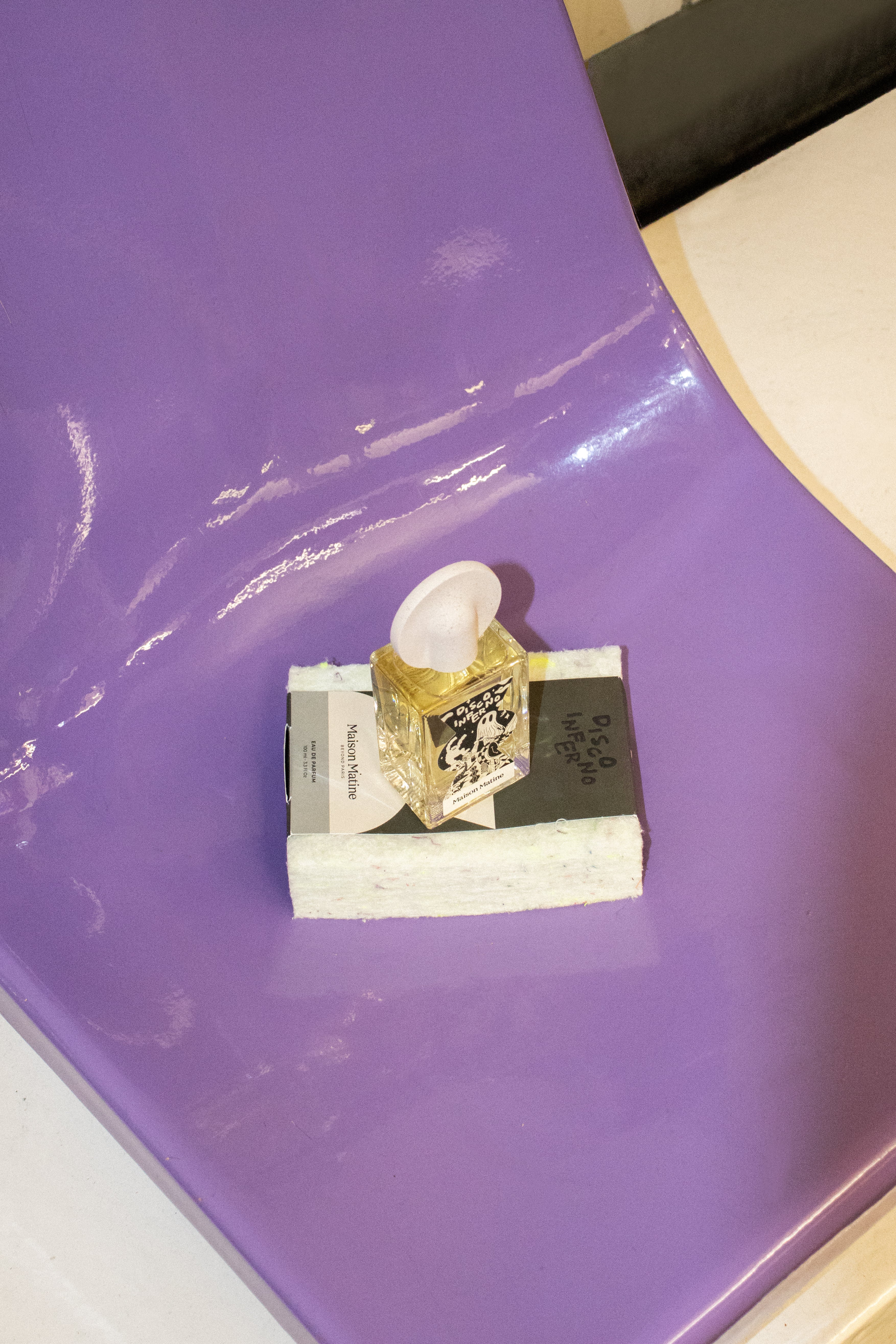 Disco Inferno perfume positioned on white packaging box against glossy purple surface with reflections
