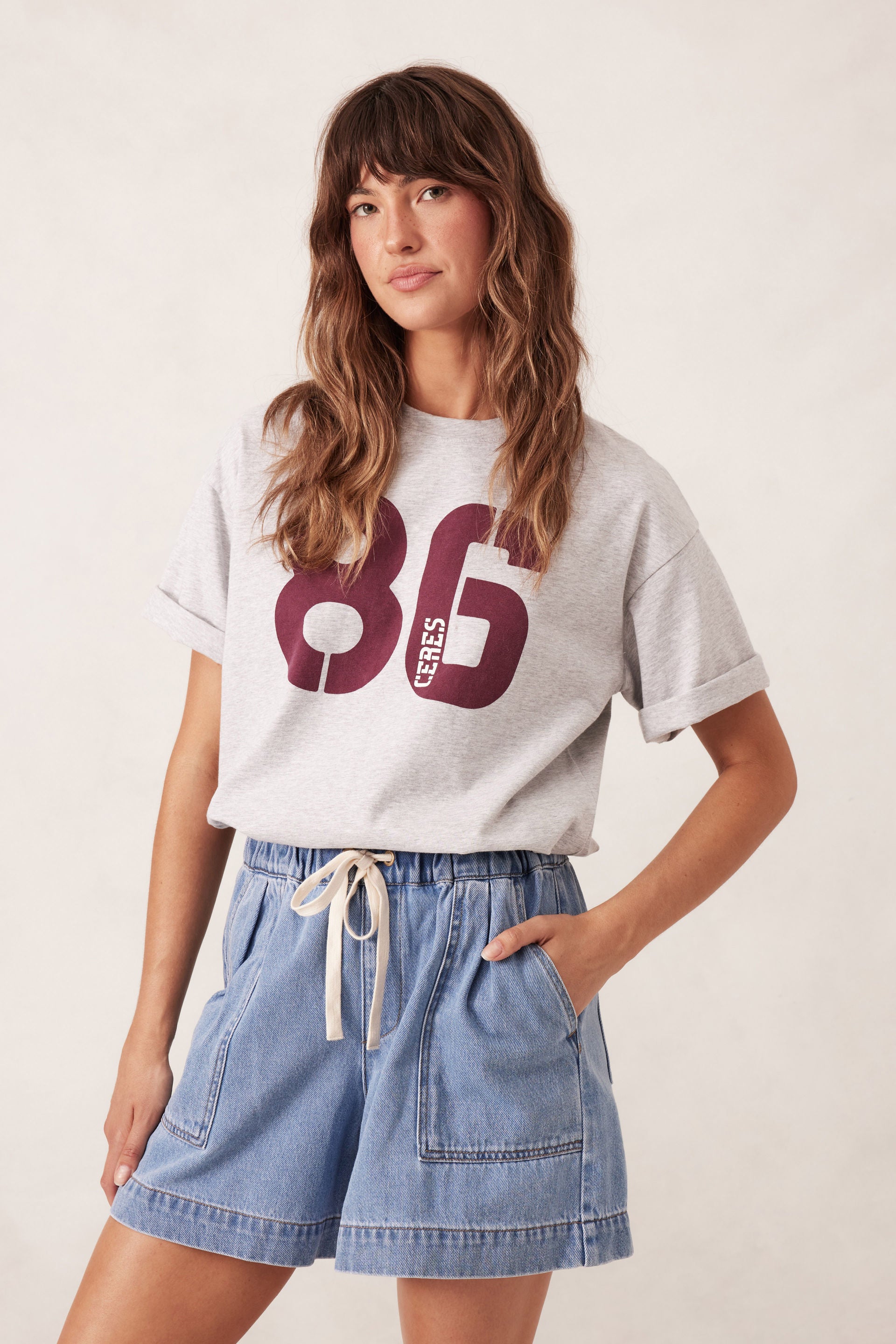 Woman wearing a white t-shirt with '86 CERES' and Ceres Life denim shorts on a plain background