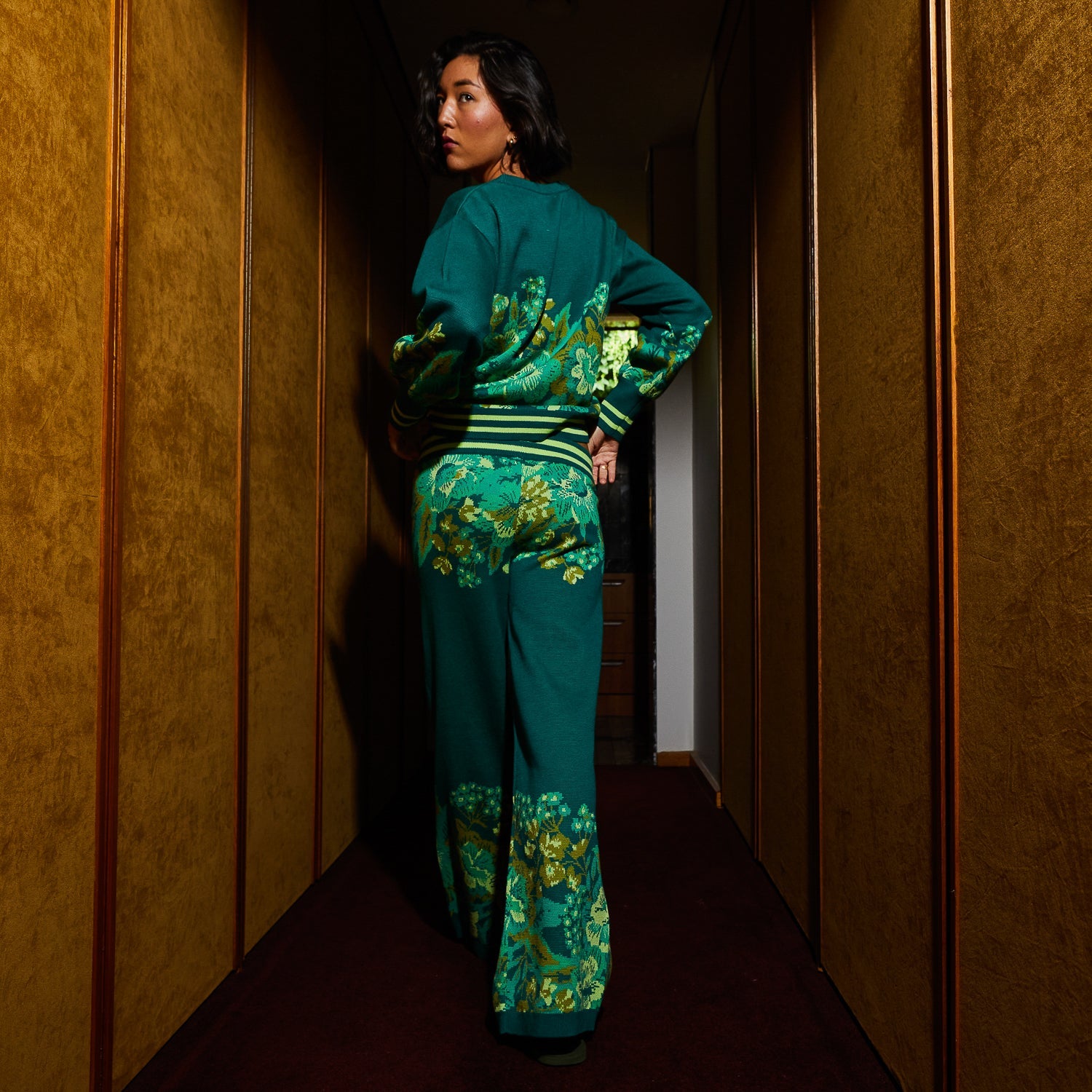 Back view of Sage & Clare Eliza Knit Pants showing floral pattern and wide leg silhouette in hallway