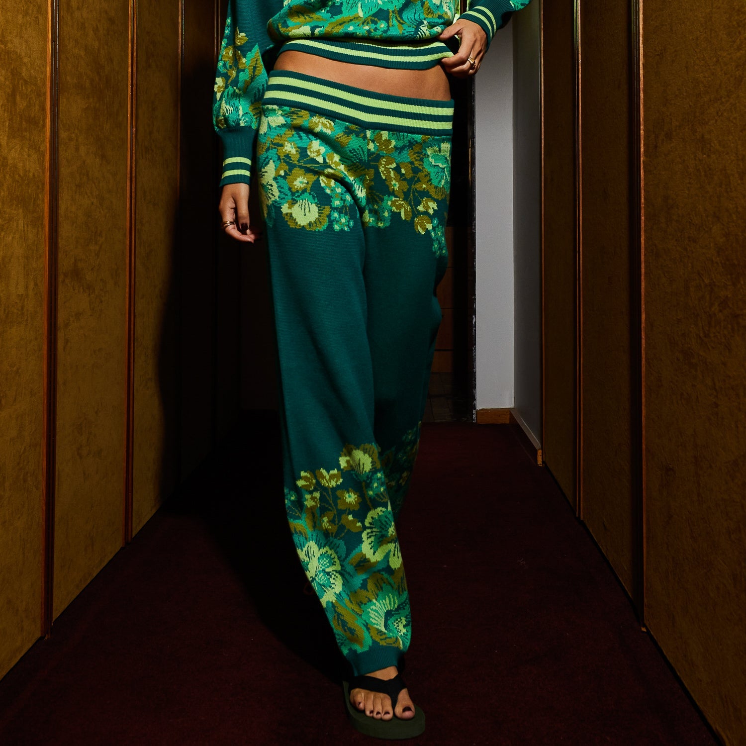 Side angle view of Eliza Knit Pants highlighting wide leg cut and floral pattern placement in hallway