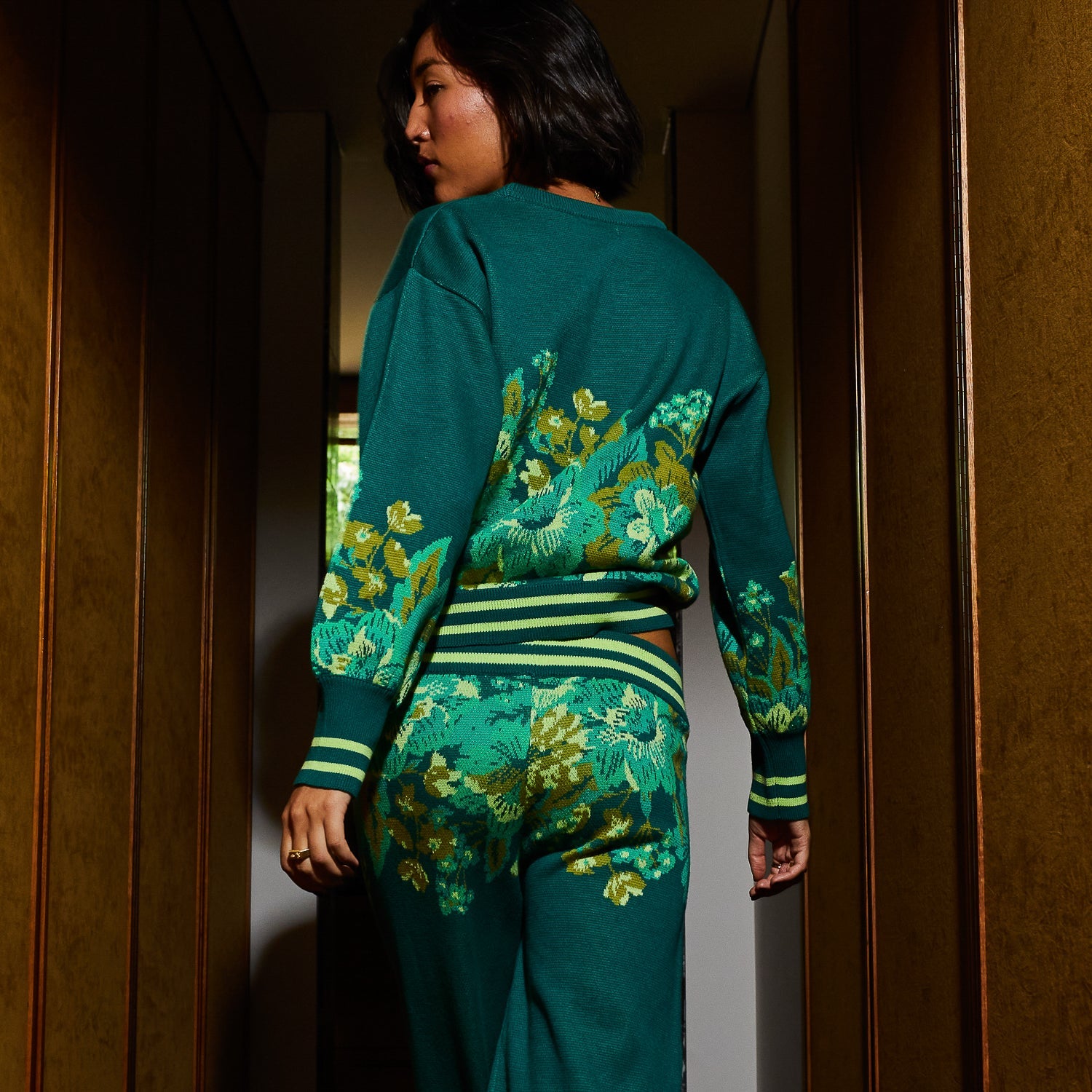Back view of model in Eliza Knit Sweater showing full botanical pattern and striped waistband