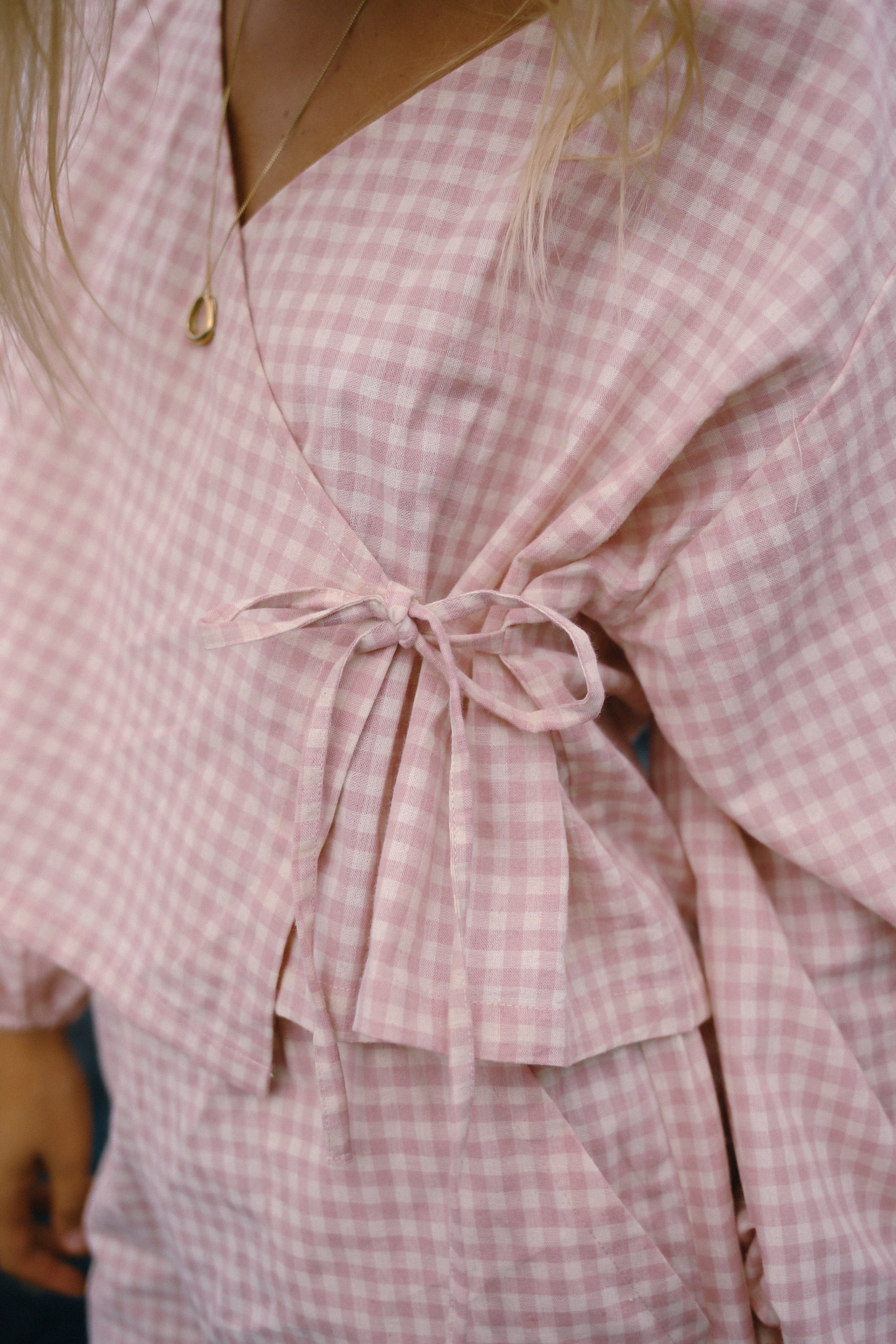 Close-up of a pink gingham wrap top with a tie waist. Made from linen and cotton