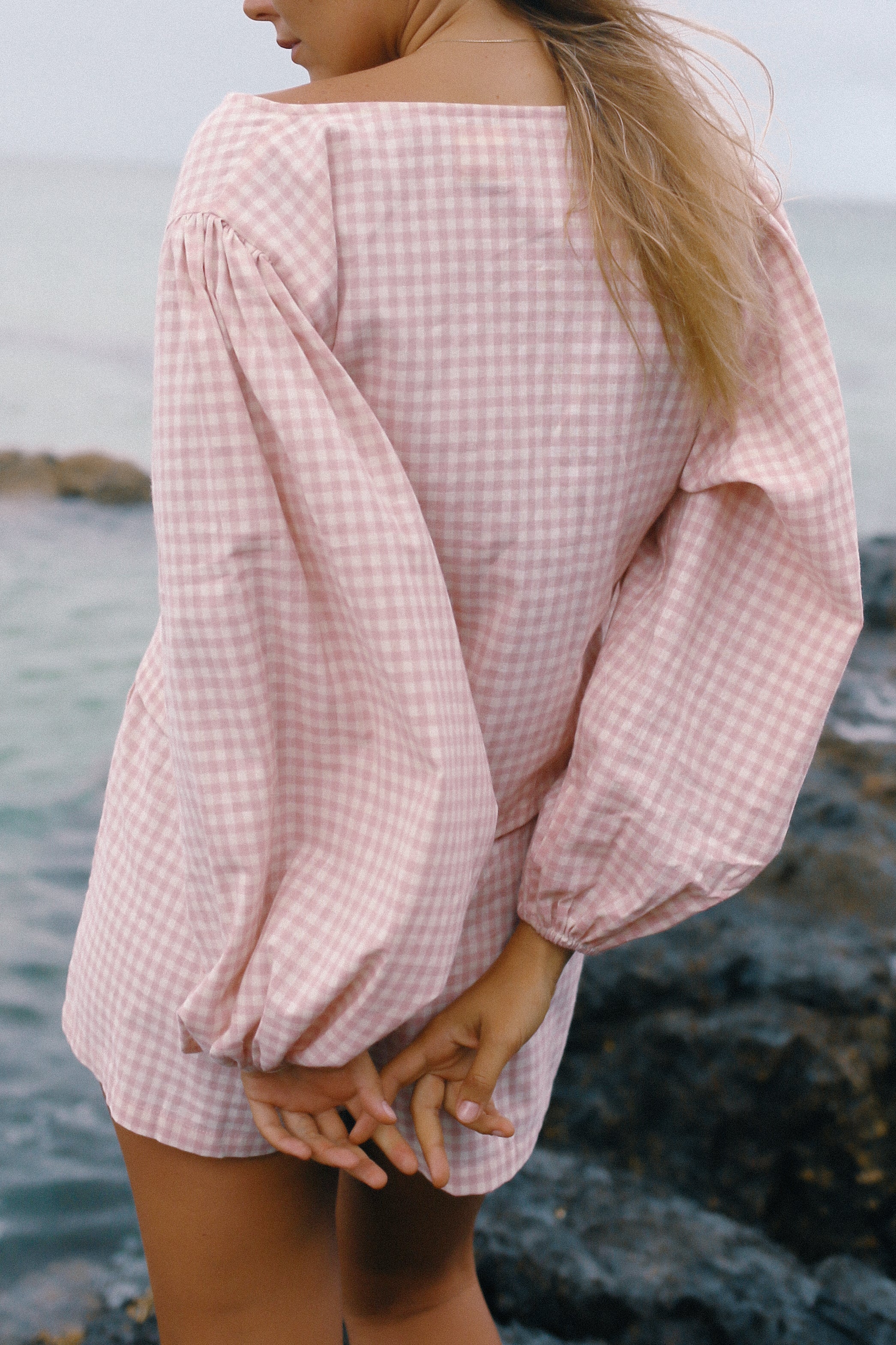 Person wearing a pink checkered long sleeve shirt by the water - Ella Wrap Top pink gingham by The Bare Road