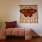 Emilia Wall Hanging displayed above cushioned bench showing orange butterfly design and cream tasseled fringe