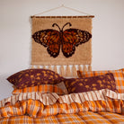 Wall hanging with butterfly design above bed showing cream background and tassel detail in bedroom setting