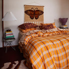 Butterfly wall hanging above bed with brown pillows showing orange and burgundy tapestry with cream fringe