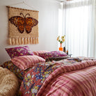 Emilia Wall Hanging above colorful patterned bedding showing butterfly design with wooden hanging hardware