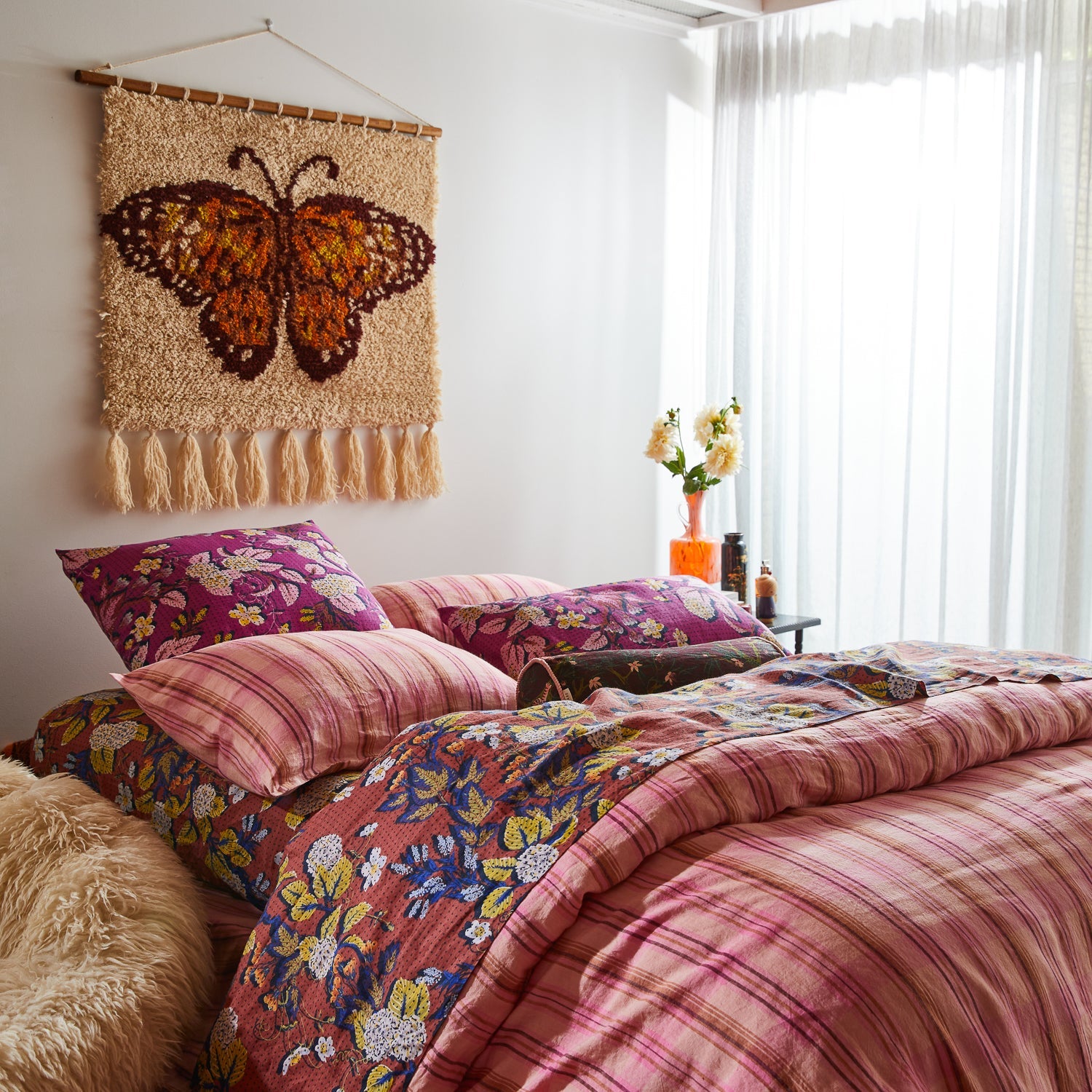 Emilia Wall Hanging above colorful patterned bedding showing butterfly design with wooden hanging hardware