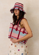 Model wearing Luxe Manhattan Hat Escape by Lorna Murray with striped burgundy pink blue brim and matching tote bag