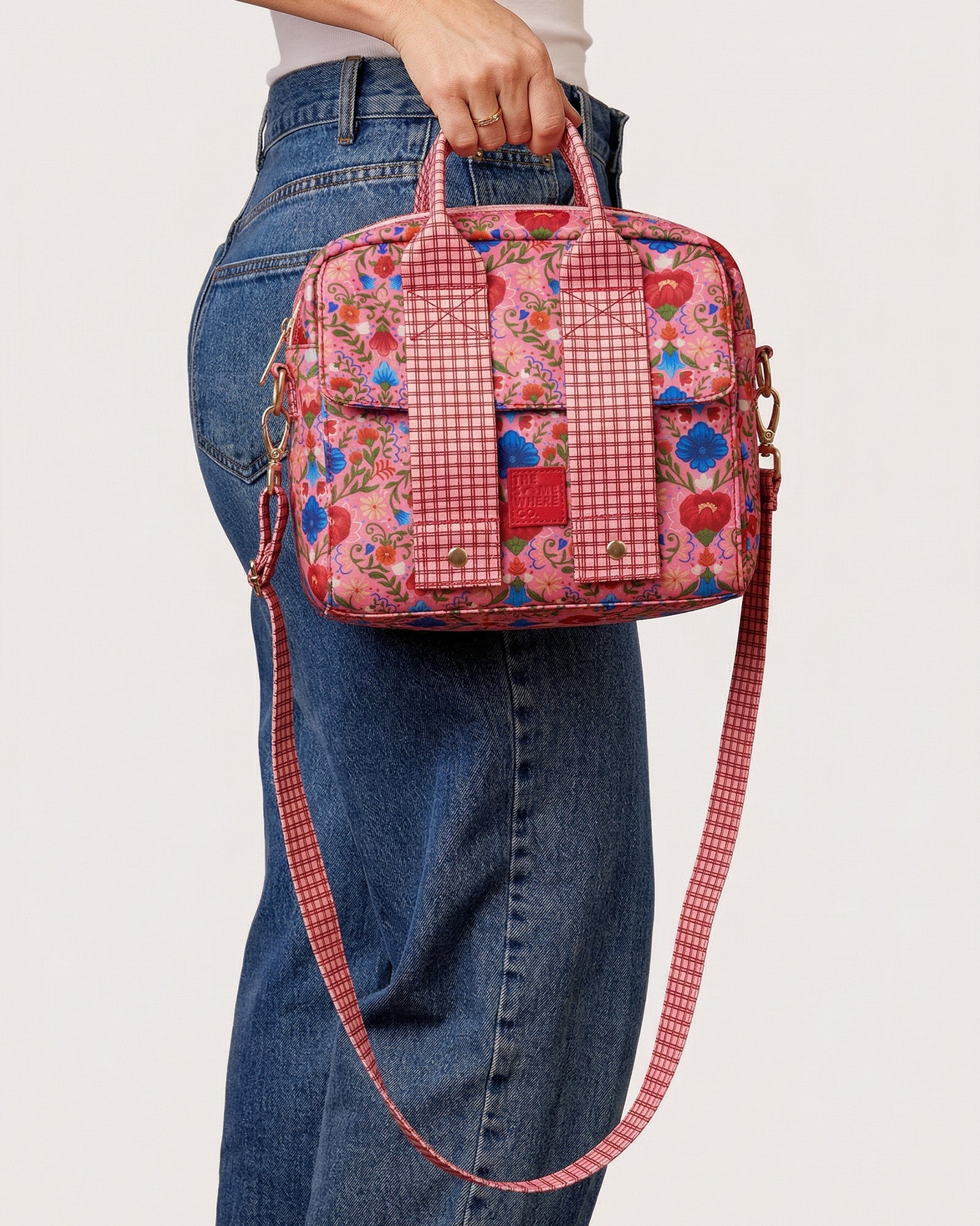 Fable lunch tote carried by hand showing floral print and gingham crossbody strap detail