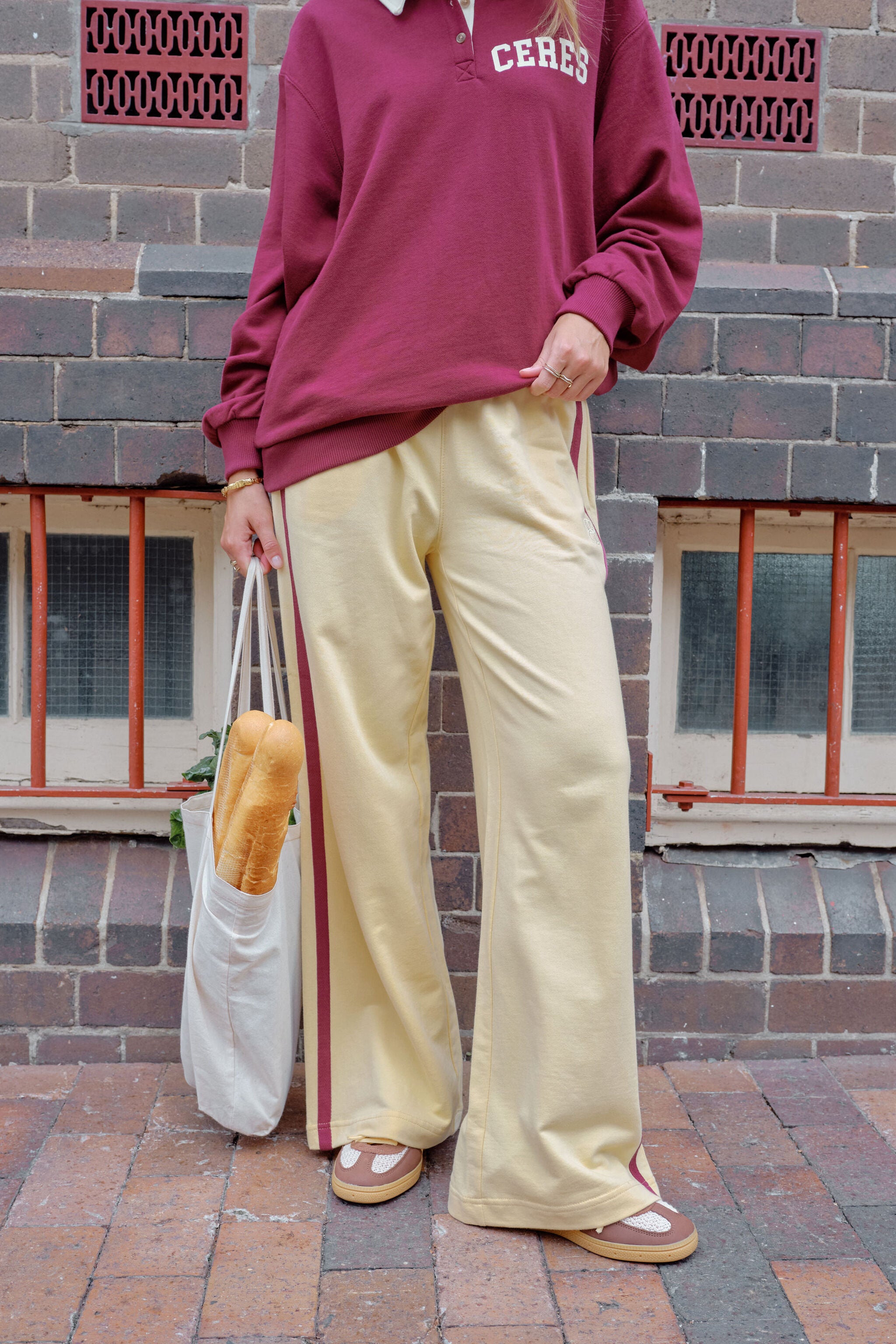 Woman sitting wearing pink wide leg track pants with white side stripe on park bench