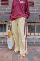 Woman wearing cream wide leg track pants with brown side stripe styled with crossbody bag