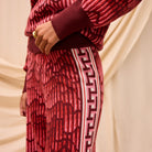 Side detail view of red knit Hanna pants showing Greek key tape trim and textured fabric