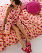 Lady sitting on bed linen in floral hibiscus pattern in orange, pink and burgundy by Kip & Co