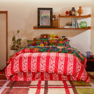 Wide bedroom shot of Ines Silk Pillowcase Verdant styled with red striped sheets and contemporary furniture
