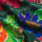 Detail view of Ines Silk Scarf fabric showing Sage & Clare branding text and intricate tropical flower print design