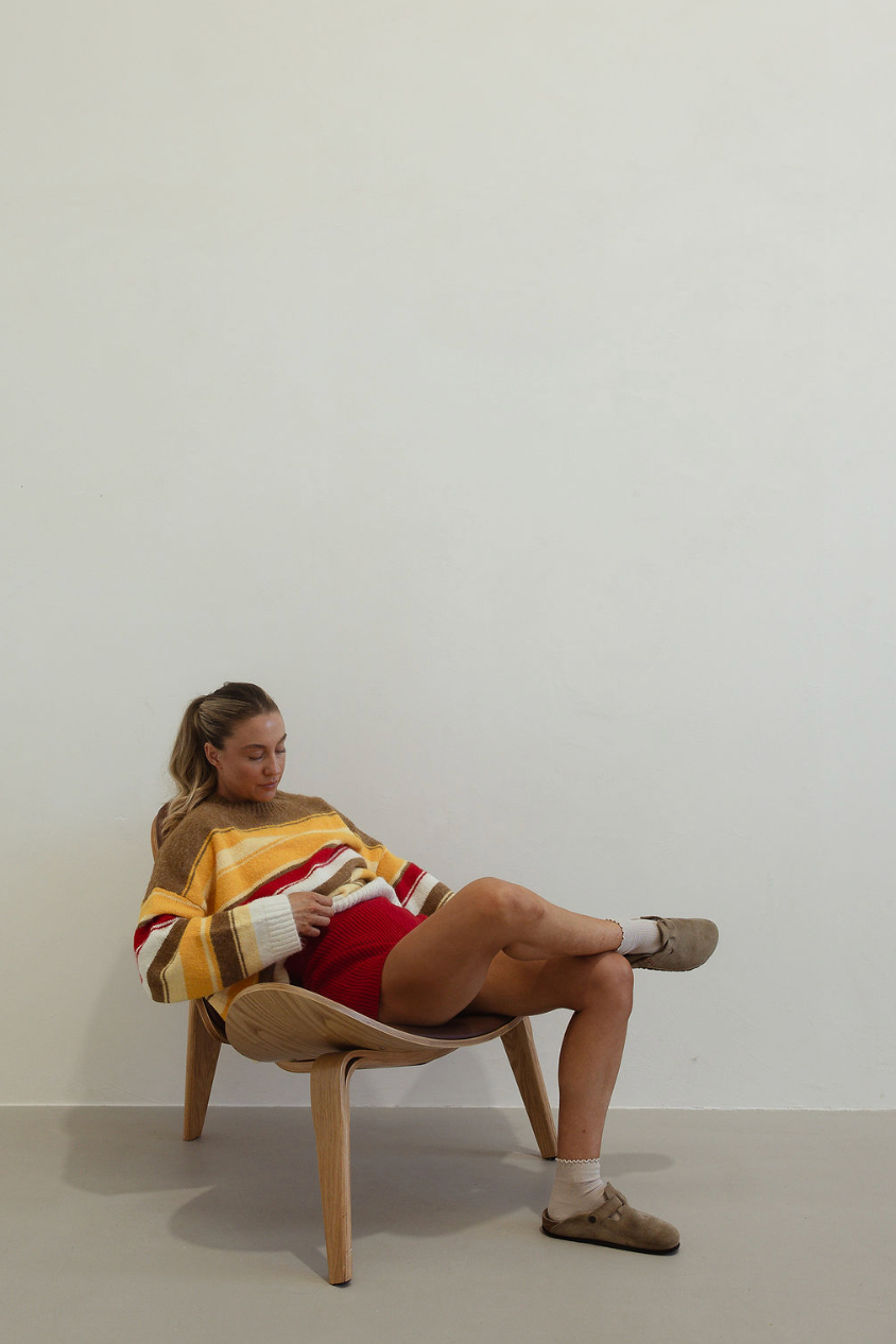 Relaxed pose showing Isabel Knit autumn stripe sweater with oversized fit and long sleeves on seated model