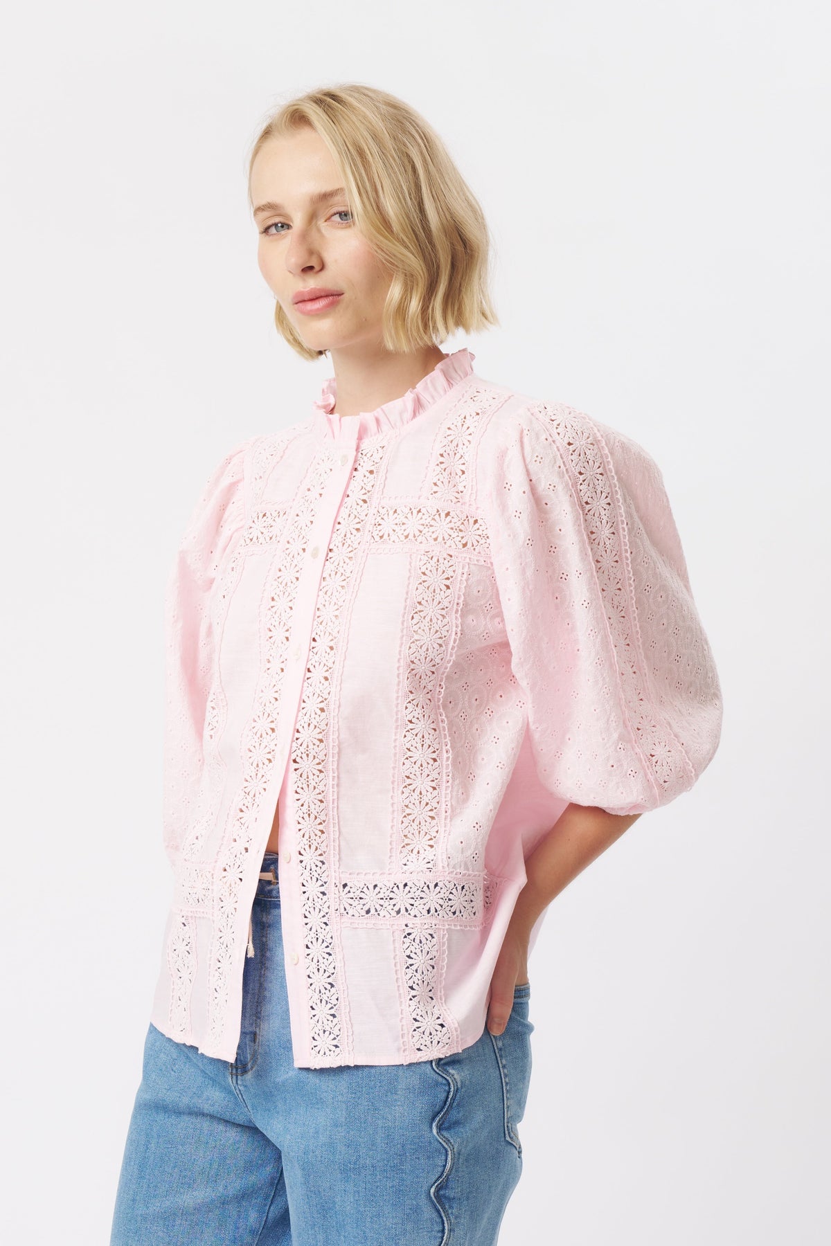 Close three-quarter front view of pink broderie anglaise shirt with puff sleeves and ruffled high neck