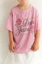 Close-up of Dear Juni tee showing rhinestone text detail and rose motif on pink fabric
