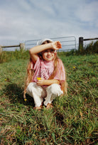 Child sitting outdoors wearing pink Dear Juni tee with rhinestone graphics in natural setting