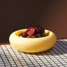Cream yellow marbled resin Jeanne Bowl holding halved plums on white tile surface with brown background